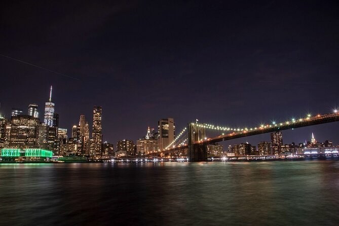 The Brooklyn Bridge lit at night with the Lower Manhattan skyline behind it, seen from the Brooklyn shore