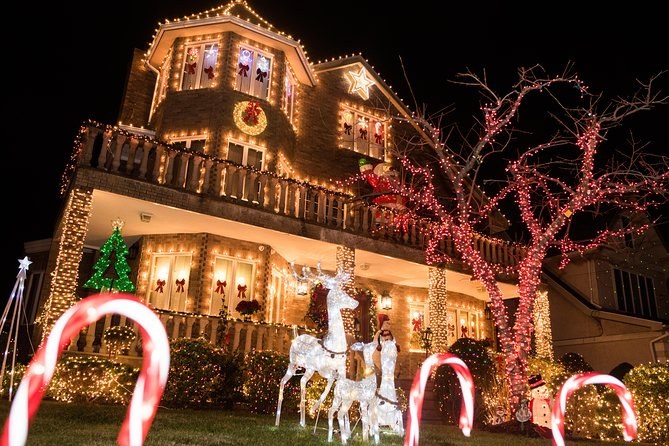 Candy canes lining the path to a lit brick house, with white reindeer on the lawn and a red-lit tree beside it
