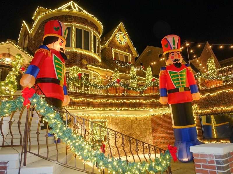 Two nutcrackers taller than a person standing at the foot of a garlanded front staircase in Dyker Heights